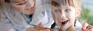 Woman dentist in protective glasses examines teeth of little girl patient with metal tools portrait