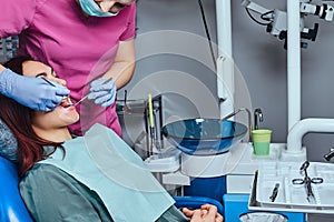 Dentist is treating female patient which is sitting in a dental chair in the clinic.