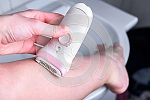 Woman depilating legs with electric epilator in bathroom.