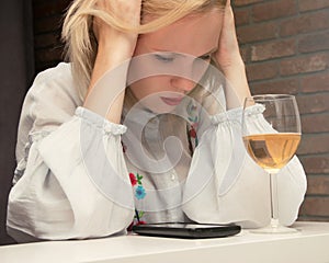 A woman in depression, feeling unwell before the phone and a glass of wine. The concept of female alcoholism