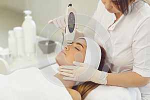 Woman dermatologist making ultrasound apparatus facial cleaning for young woman