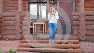 Woman Descends The Stairs From The Porch Of Wooden House And Holds A Cup Of Tea