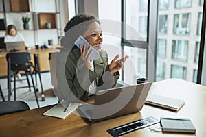 Woman at desk with laptop, talking on cell phone in office setting