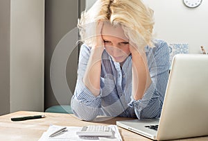 Woman at desk Stares at Calculator Holding Head in Hands