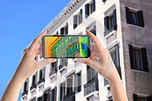 Woman detecting heat loss in building using thermal viewer on smartphone. Energy efficiency