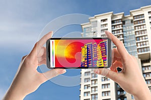 Woman detecting heat loss in building using thermal viewer on smartphone. Energy efficiency