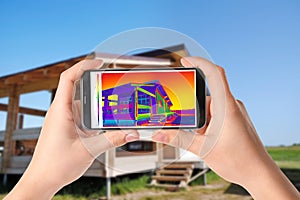 Woman detecting heat loss in house using thermal viewer on smartphone. Energy efficiency