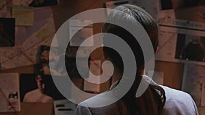 Woman detective looking at board with crime information and drinking coffee