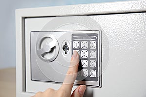 Woman dialing combination on keypad of steel safe, closeup