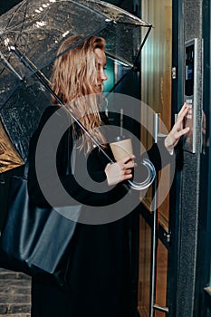 Woman dialing a number on the on video intercom at entrance of apartment building in the night