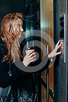 Woman dialing a number on the on video intercom at entrance of apartment building in the night