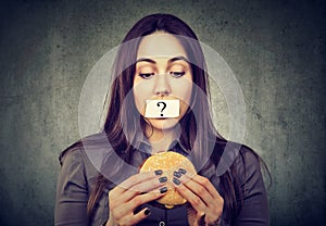 Woman on diet restriction with question mark on mouth looking at burger