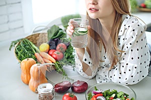 Woman on a diet. Young and happy woman eating healthy salad sitting on the table with green fresh ingredients indoors