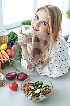 Woman on a diet. Young and happy woman eating healthy salad sitting on the table with green fresh ingredients indoors