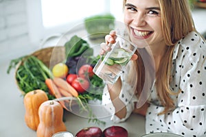 Woman on a diet. Young and happy woman eating healthy salad sitting on the table with green fresh ingredients indoors