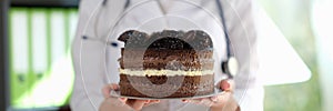 Woman dietician holds big slice of chocolate cake with cream.