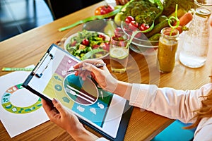 Woman dietitian in medical uniform with tape measure working on a diet plan sitting with different healthy food ingredients in the