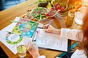 Woman dietitian in medical uniform with tape measure working on a diet plan sitting with different healthy food ingredients in the photo