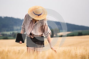 Woman with digital tablet examining quality of cereal plant