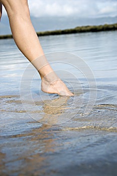 Woman dipping toe in water.