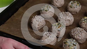 A woman dips a ball of dough in seeds and puts it on a baking sheet. Makes whole grain buns. Close-up