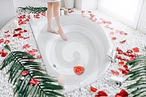 Woman dips legs into the bath, rose petal decor
