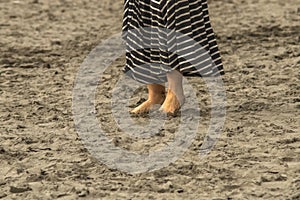 Woman with dirty feet and toes dug into the sand on the beach with longish dress - bottom one third of body - close-up and