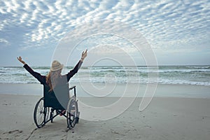 Woman disable sitting with open arm on wheelchair at beach