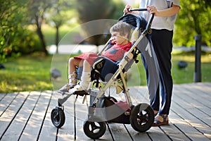 Woman with disabled girl in a wheelchair walking in the Park summer. Child cerebral palsy. Family with disabled kid photo