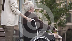 Woman with disabled grandfather in wheelchair walking in park, volunteering