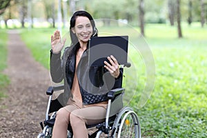 Woman disabled operator in headphones with microphone and laptop works in wheelchair in park