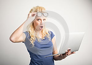 Woman in disbelief lifting up her glasses and holding laptop
