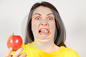 A woman with a disgruntled grimace of pills on her tongue holds an apple. Rejection of synthetic dietary supplements and