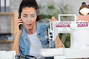 woman with dismantled sewing machine making call on smartphone
