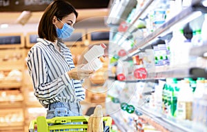 Woman in disposable mask shopping groceries, buying milk