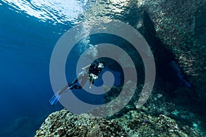 woman diver underwater at the entrance of a cave with sunrays