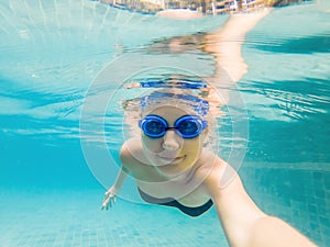 A woman with diving glasses is swimming in the pool under the water