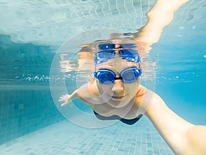 A woman with diving glasses is swimming in the pool under the water