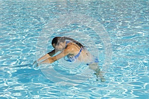 Woman diving in the swimming pool. Young beautiful girl swimming in pool. Brunette relaxing in clear warm water on sunny day. Top