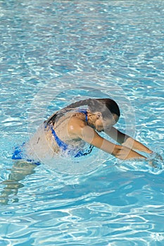 Woman diving in the swimming pool. Young beautiful girl swimming in pool. Brunette relaxing in clear warm water on sunny day. Top