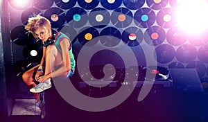 Woman, dj and portrait on stage with turntable in night club, sitting and wall of vinyls for music event. Female photo