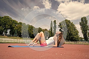 Woman do pilates on yoga mat. Sensual woman relax on stadium. Fashion athlete practice yoga outdoor. Wellness and