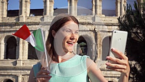 Woman do selfie on mobile near Colosseum in Rome, Italy. Teenager wave Italian flag in slow motion