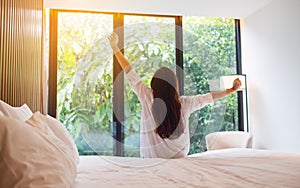 A woman do stretching after waking up in the morning  , looking at a beautiful nature view outside bedroom
