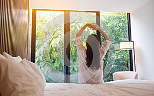 A woman do stretching after waking up in the morning  , looking at a beautiful nature view outside bedroom