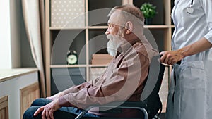 Woman doctor assist unhealthy elderly grandfather patient in wheelchair approaching to window