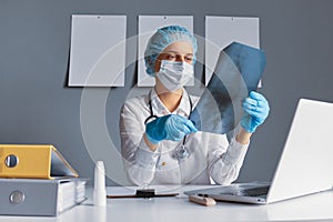 Woman doctor conducts an online consultation examining patient X-ray films and MRI scans at a table with a laptop in stuff room