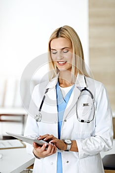 Woman-doctor controls medication history records and exam results while using tablet computer in sunny hospital