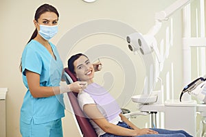 Woman doctor dentist and positive woman patient looking ar camera during tooth examination