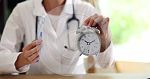 Woman doctor dentist working in clinic holding toothbrush and an alarm clock